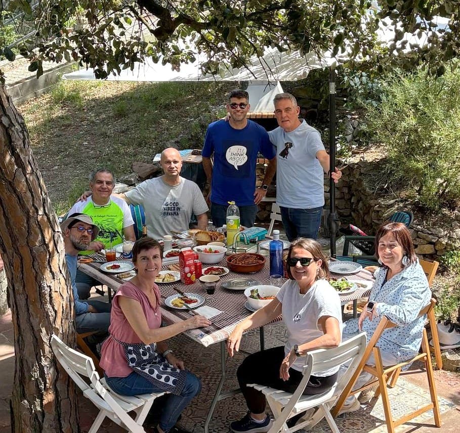 Les vuit persones voluntàries de l'Associació Sunday, al voltant d'una taula parada en una terrassa a l'ombra d'un pi.